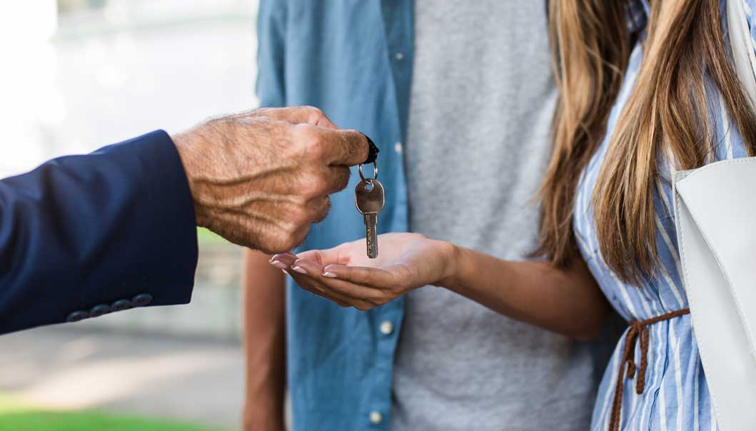 A suit sleeved man hands over a key to a woman.